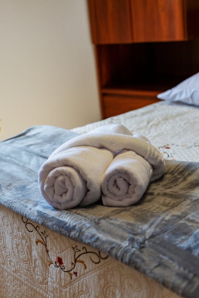 Elegant hotel room featuring rolled white towels on a neatly made bed, evoking comfort and luxury.